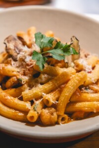 A dish of sedanini alla norma with Cherry tomato, golden fried eggplants, pecorino romano, basil, garlic and onion